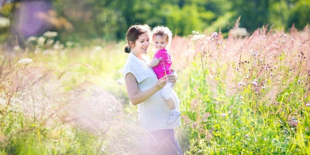 Pregnant mother and her toddler walking in a sunny meadow